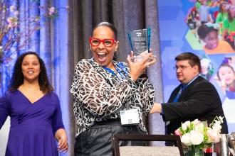 A paraprofessional accepts an award and is all smiles at the 2024 UFT Paraprofessional Festival and Awards Celebration.