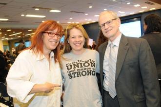 Two women and a man pose for photo displaying a grey t-shirt