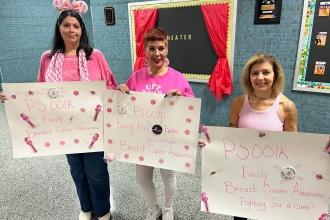 A group of staff at a public school in Brooklyn show off their signs for breast cancer awareness