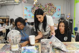 An art teacher hands out art supplies to her students in a classroom.