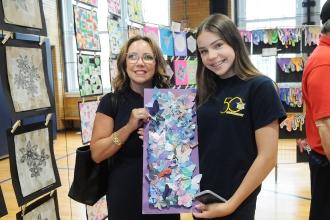 A mother and her daughter pose for a photo with the daughter's butterfly collage at the IS 34 art show on Staten Island.
