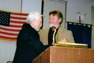 Two men at a podium and one is receiving an award 