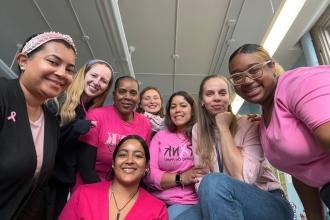 A group of staff at a public school in the Bronx gather for a selfie while wearing matching pink attire for breast cancer awareness.